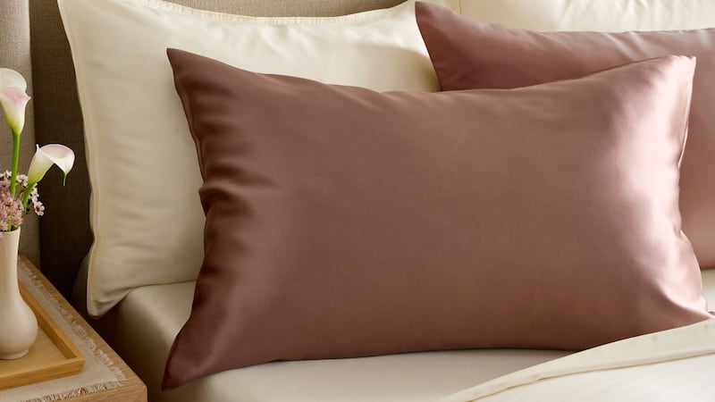 A Quince Silk Pillowcase on a bed with complementary bedding.