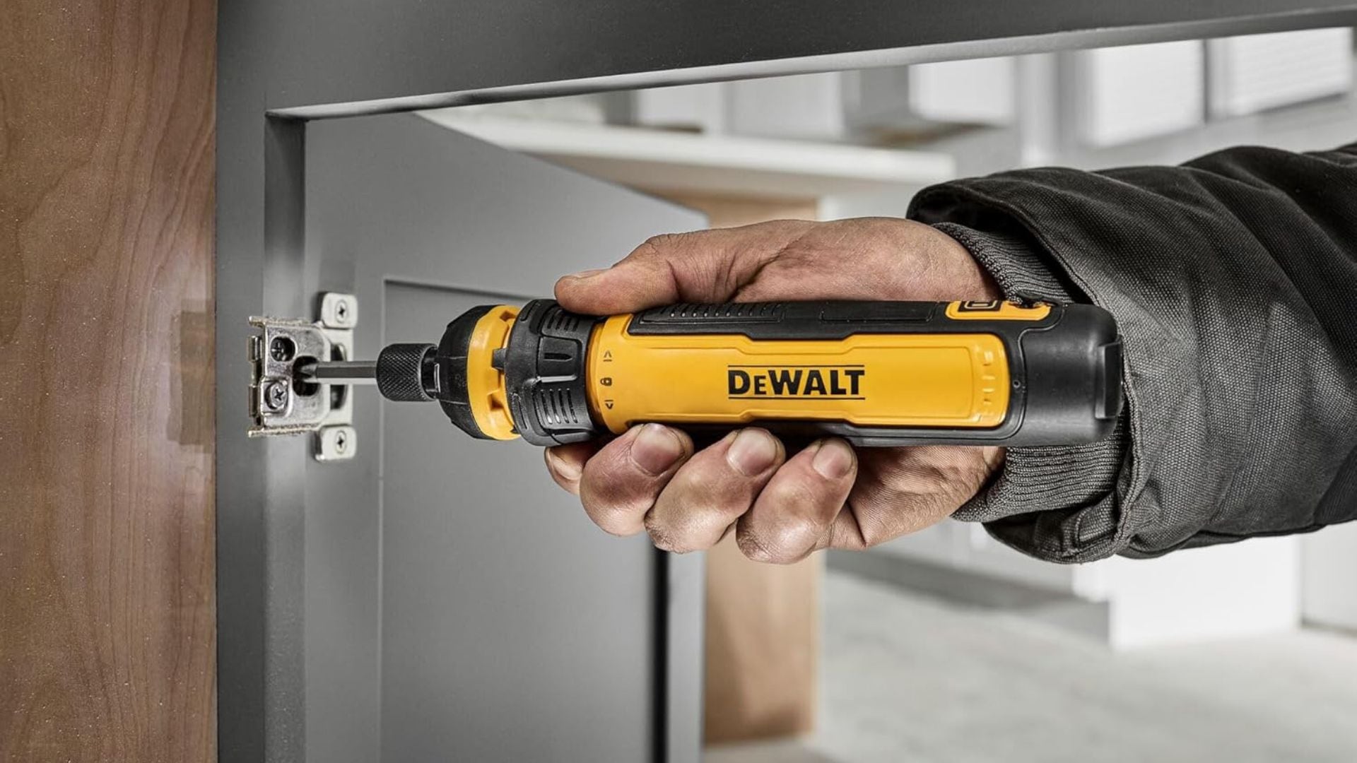 A person using the DeWALT cordless screwdriver to screw in a cabinet door.