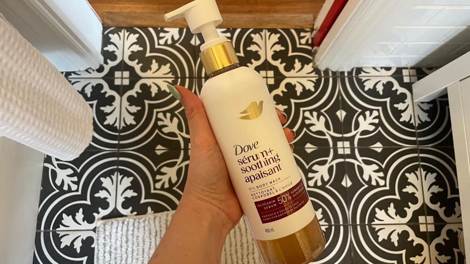 Alice is holding a bottle of Dove body wash over a tiled bathroom floor.