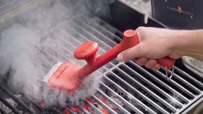 A person cleaning a grill with the ThermoMaven BBQ Grill Brush.