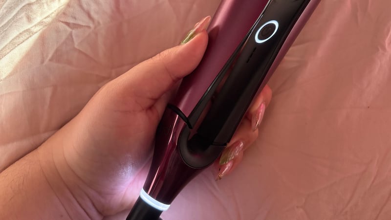 Bianca's hand holding the flat iron which is lit up to indicate the iron is on