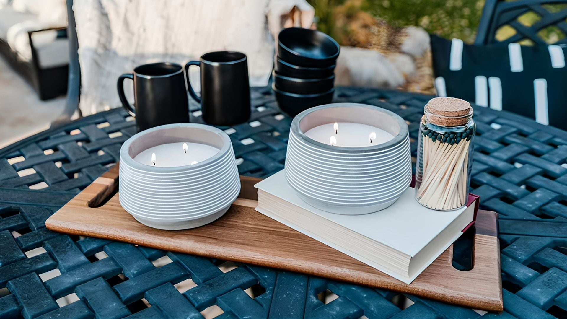 two candles on a wooden board sitting on an outdoor table