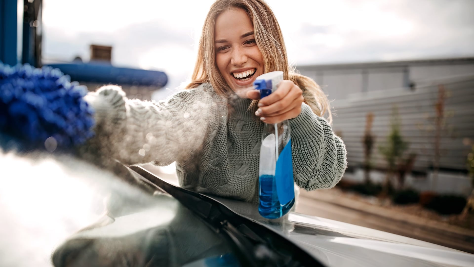 Woman cleaning the window car with a blue liquid spray bottle