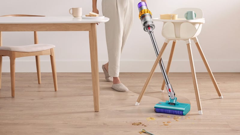 A person using a Dyson vacuum to clean a hardwood floor.