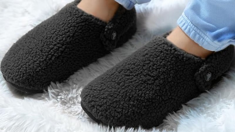 A person sitting on a fluffy rug wearing sweatpants and Crocs slippers.