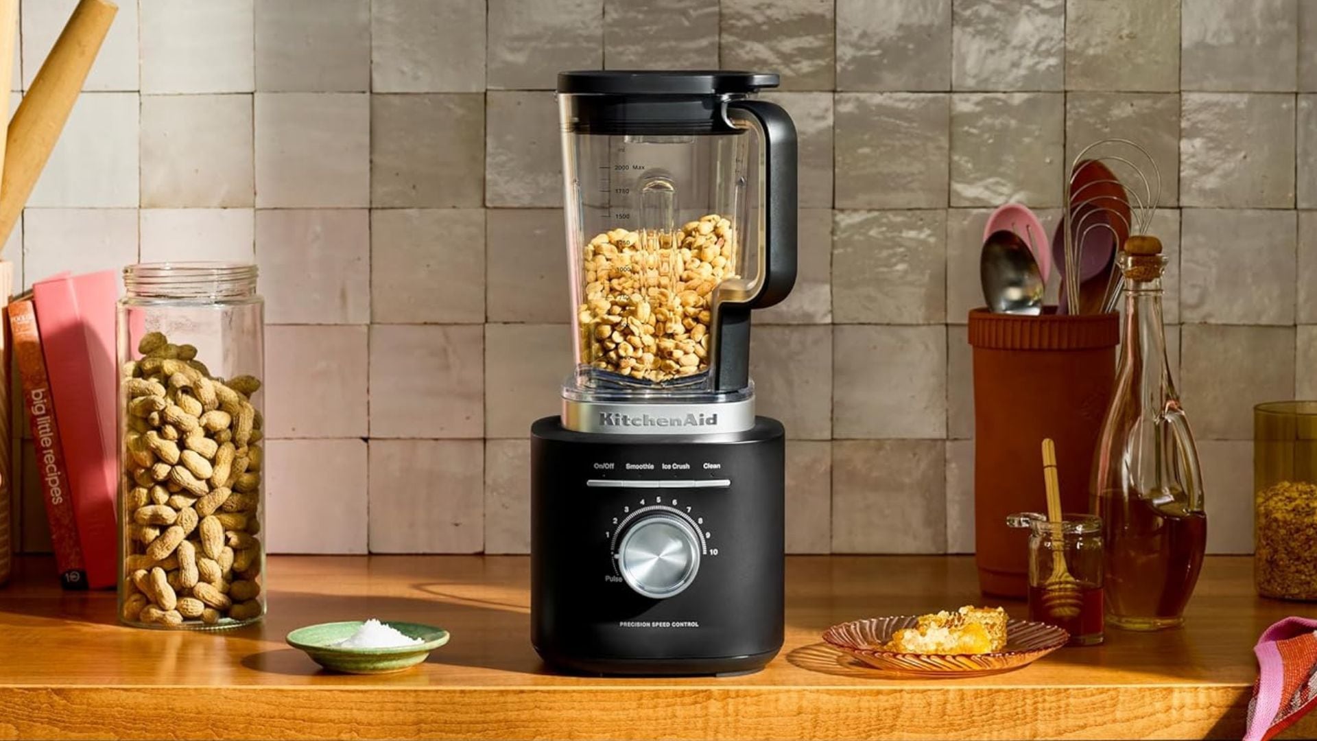 A KitchenAid blender filled with cashews on a wooden countertop.