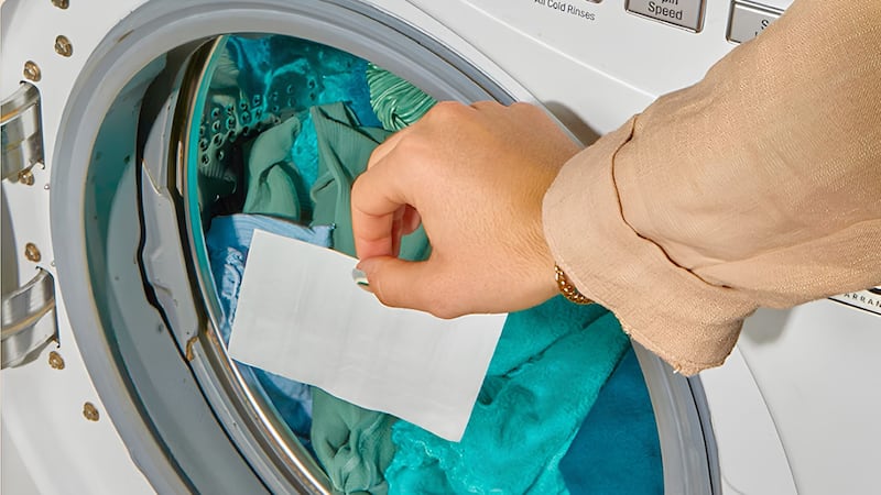 A person putting a Kind Laundry strip into a loaded washing machine.