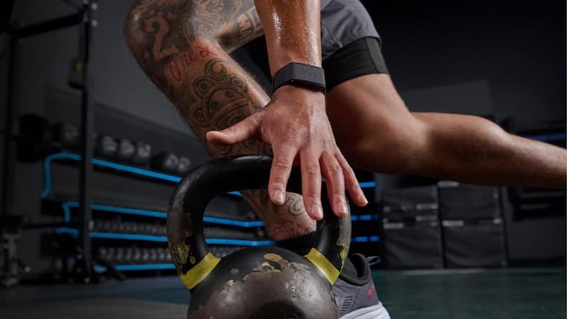 A person wearing a Amazfit Helio Strap Screenless Activity Tracker and picking up a kettlebell.
