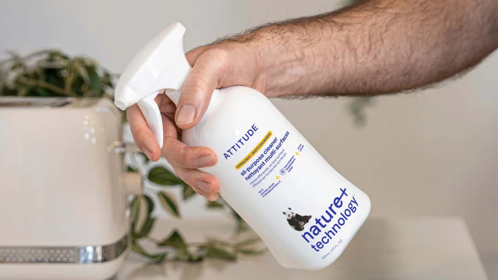 A person holding a bottle of ATTITUDE cleaning spray.