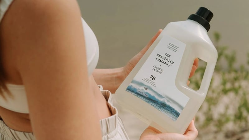 A person holding a jug of detergent from The Unscented Company.