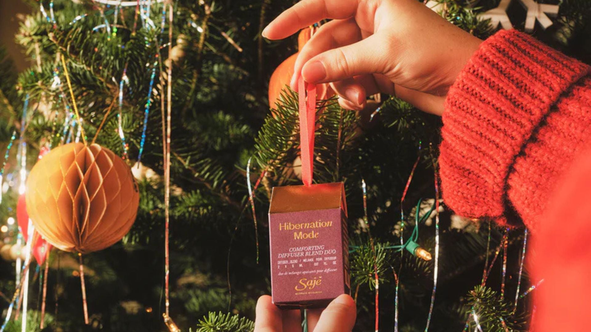 A person putting a Saje ornament gift onto a tree.