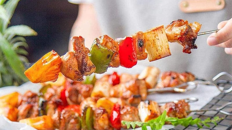 A person holding a vegetable and chicken skewer.