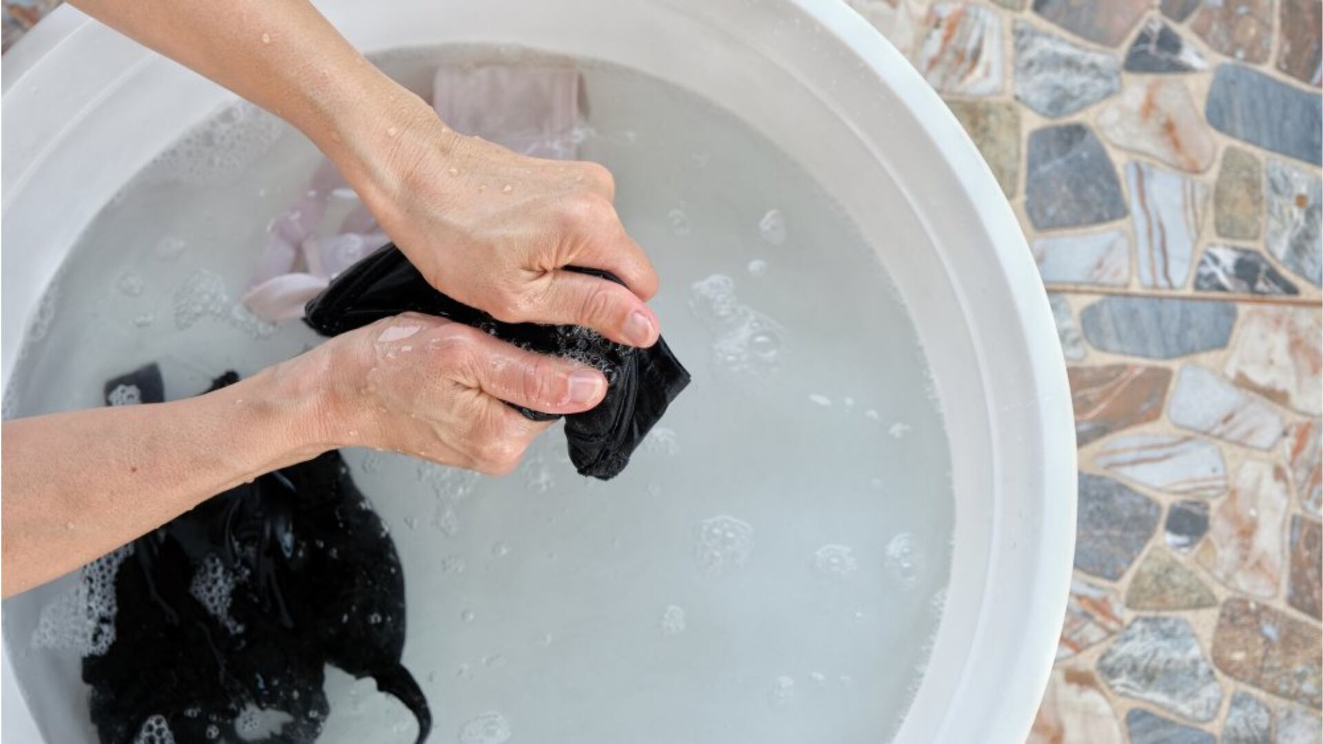 Someone hand-washing dark clothes on top of a water bin