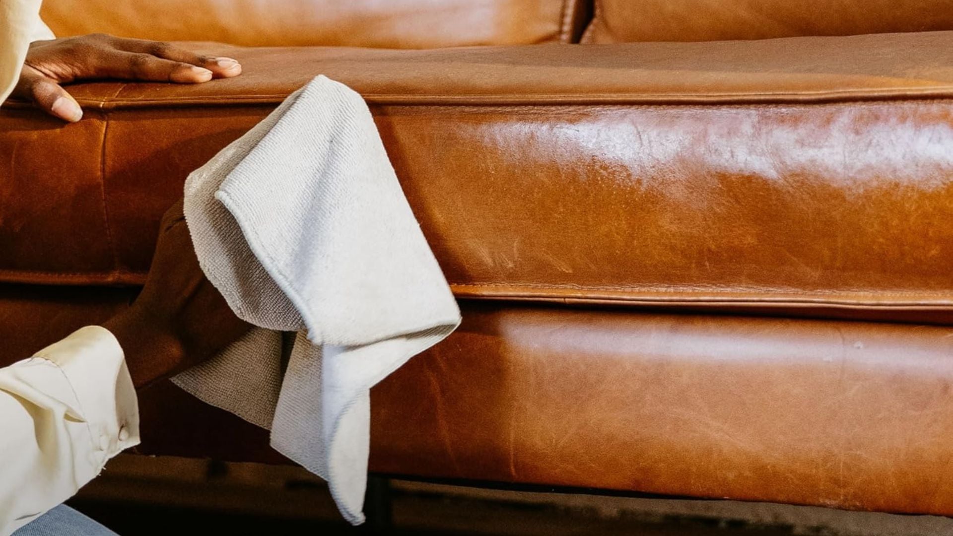 A person using Leather Honey Leather Conditioner to clean a leather couch.