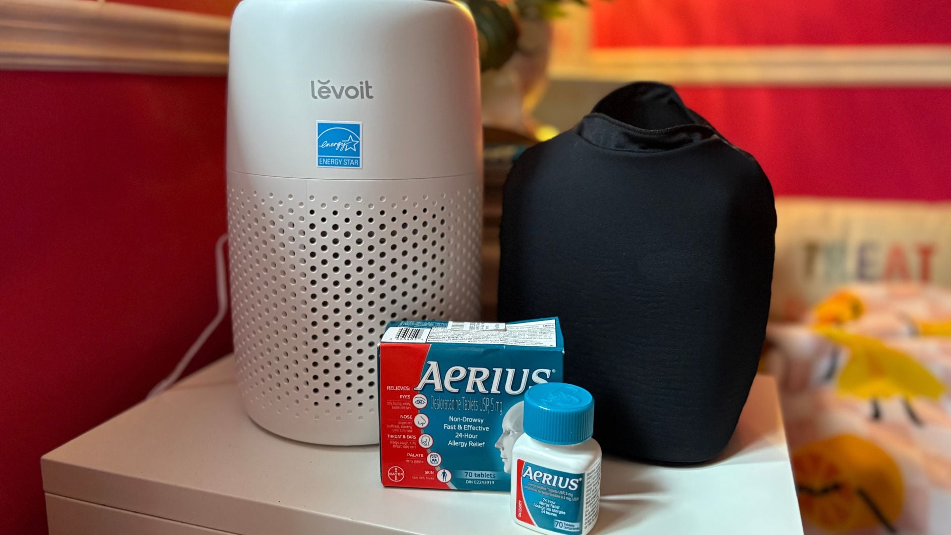 an air purifier, allergy medication, and a migraine hat on a table with a lamp behind it