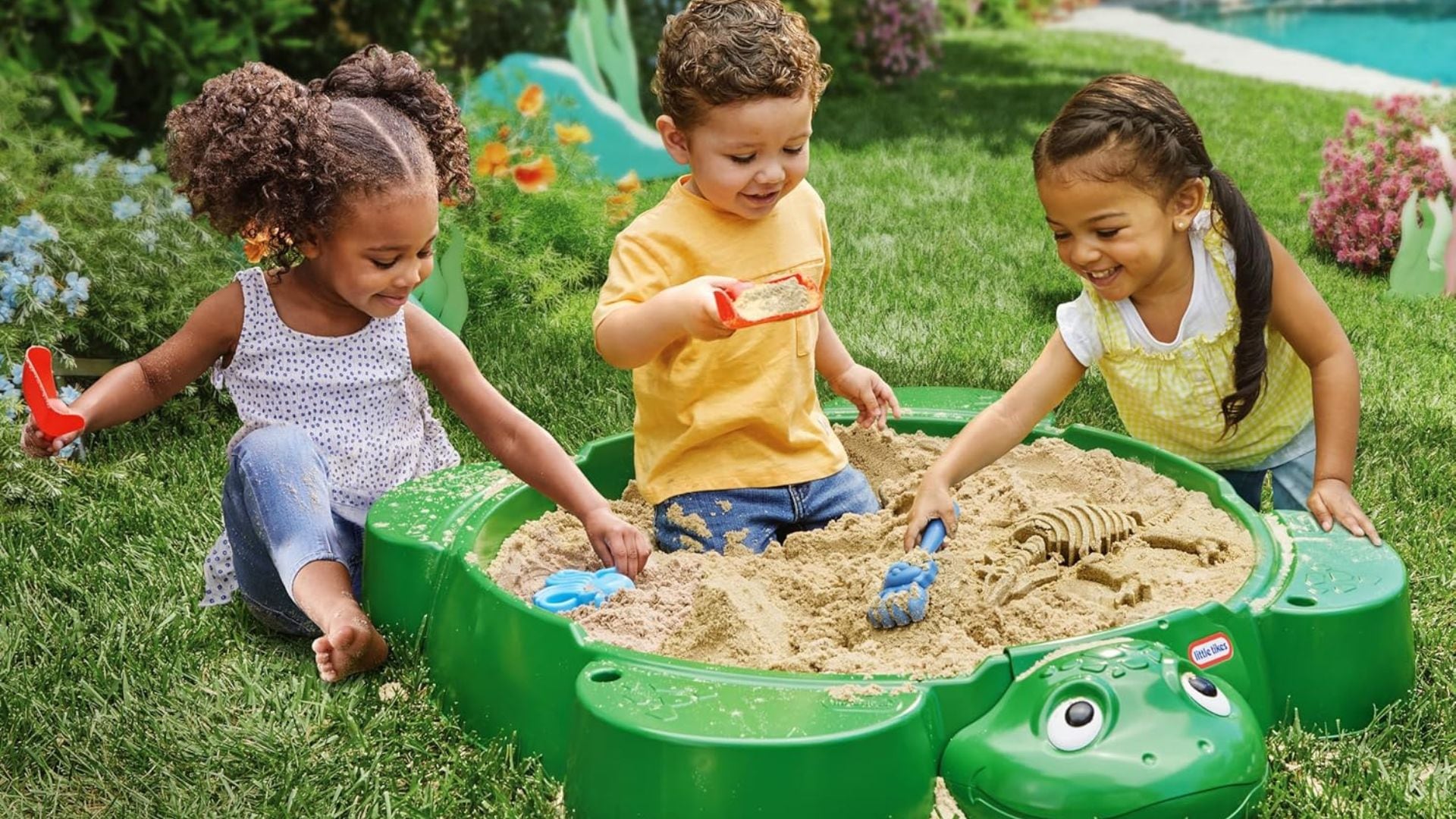 three children playing in a turtle sandbox outside