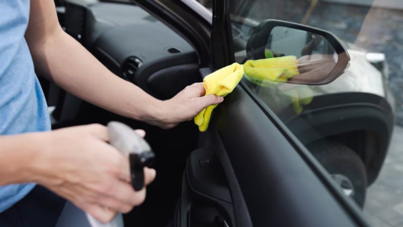 Person wiping the interior of a car door with a yellow cloth