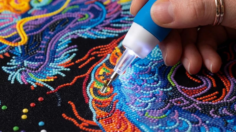 A person using a Diamond Dotz tool to complete a diamond art dragon.