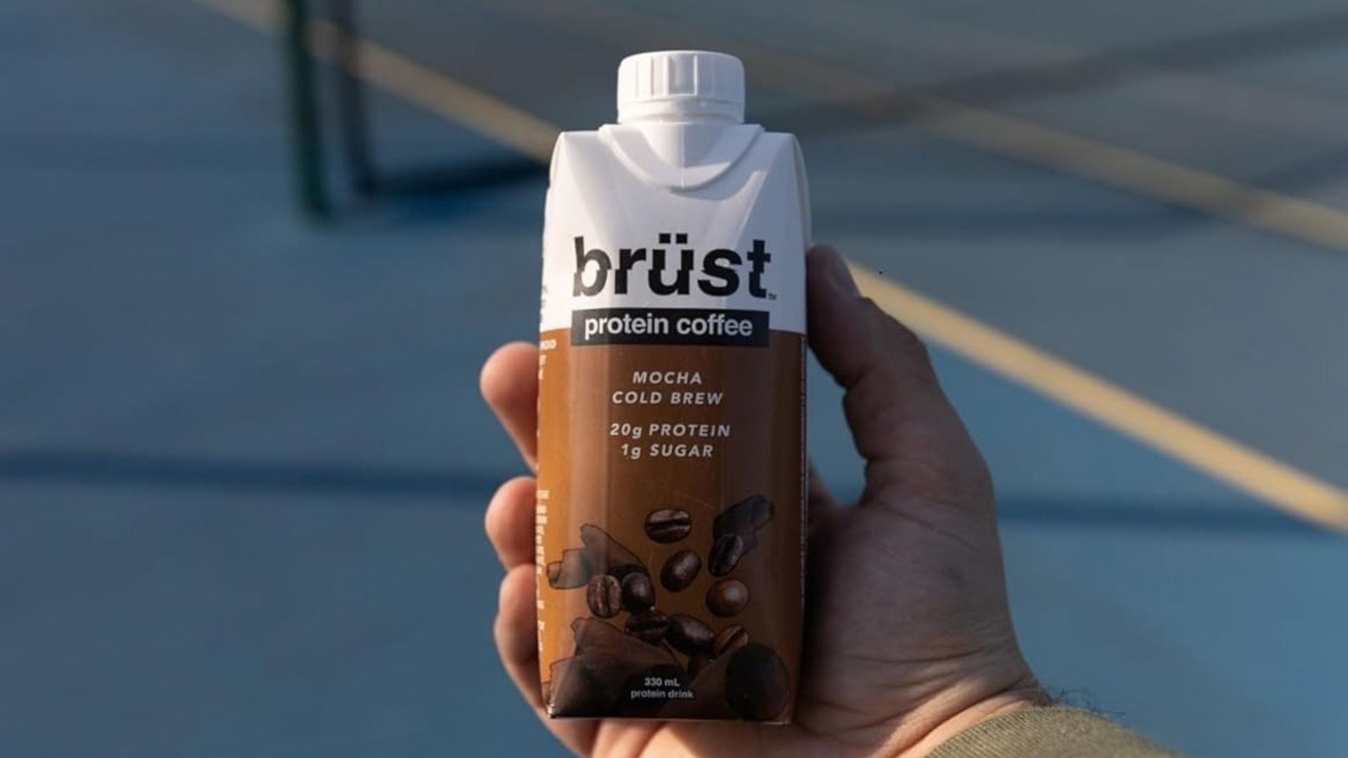 a person holding the protein drink on a tennis court