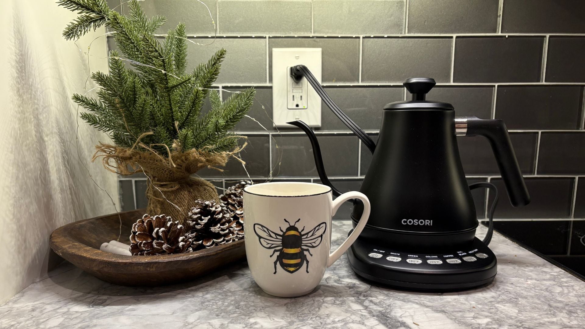 The kettle on a marble countertop next to a mug and some winter decor