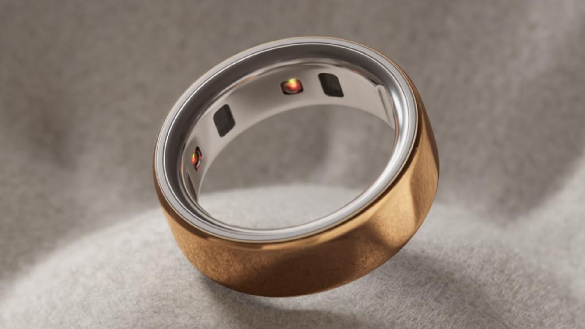 A rose gold OURA ring on a grey background.