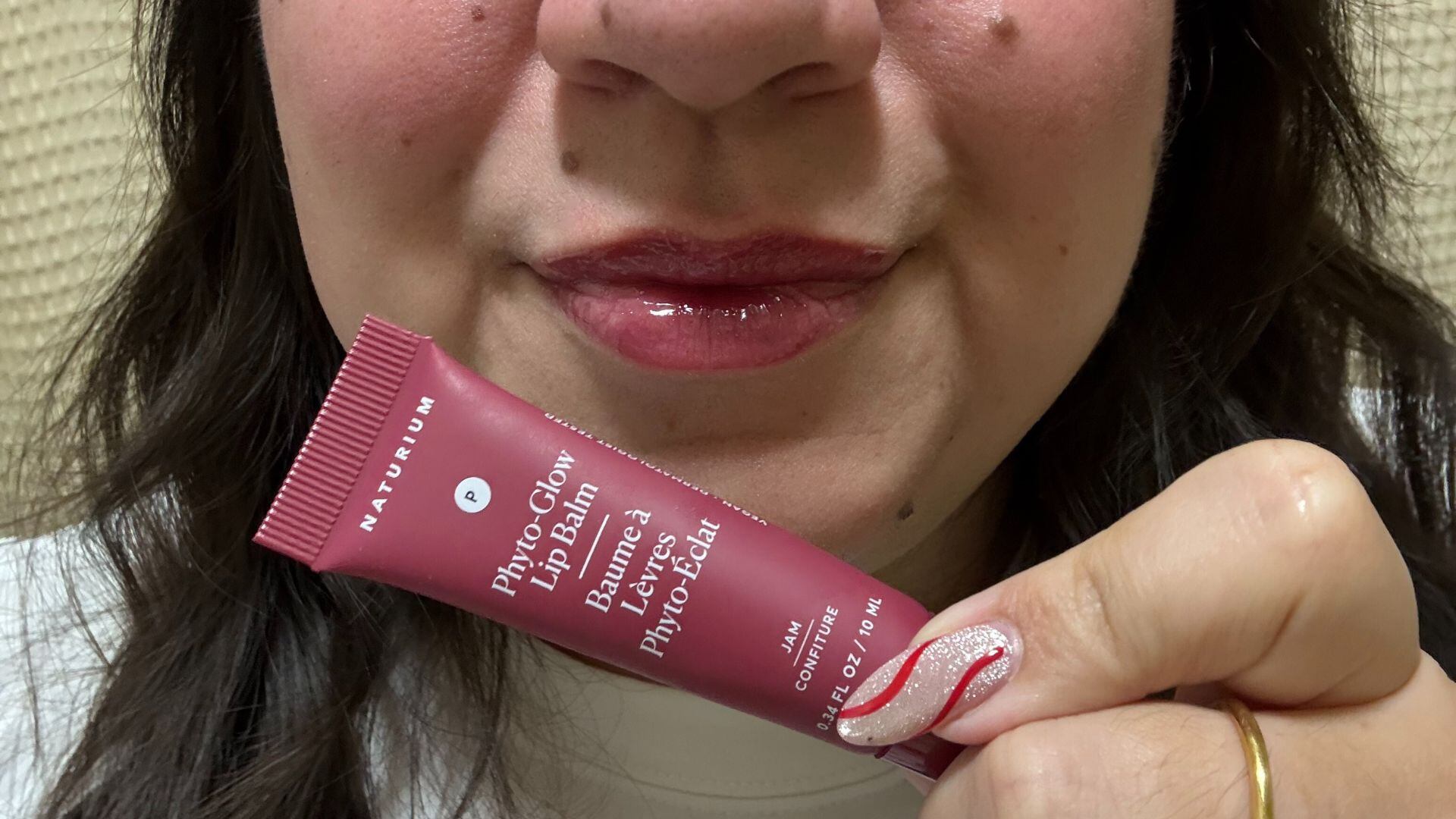 Bianca with the gloss on her lips holding up a tube of gloss