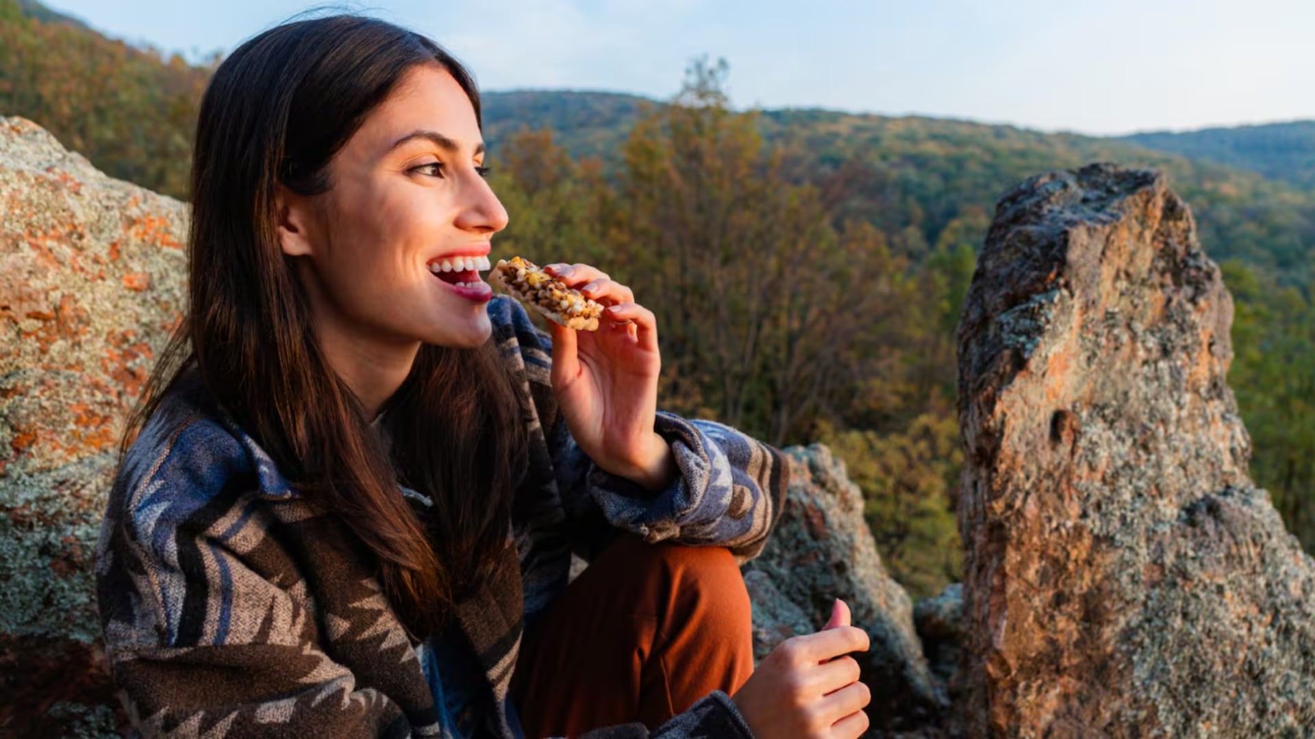 Woman eating a protein bar on top of a mountain