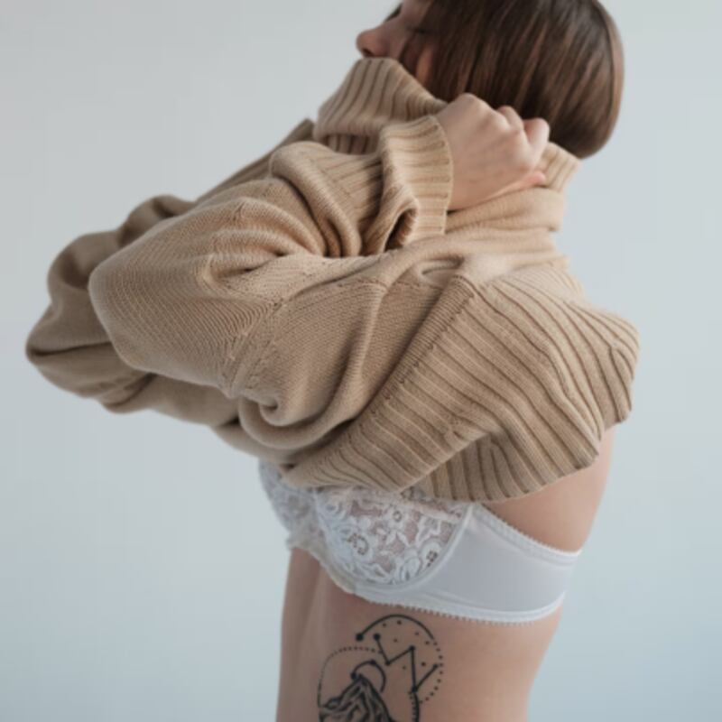 Model putting on a beige turtle neck sweater