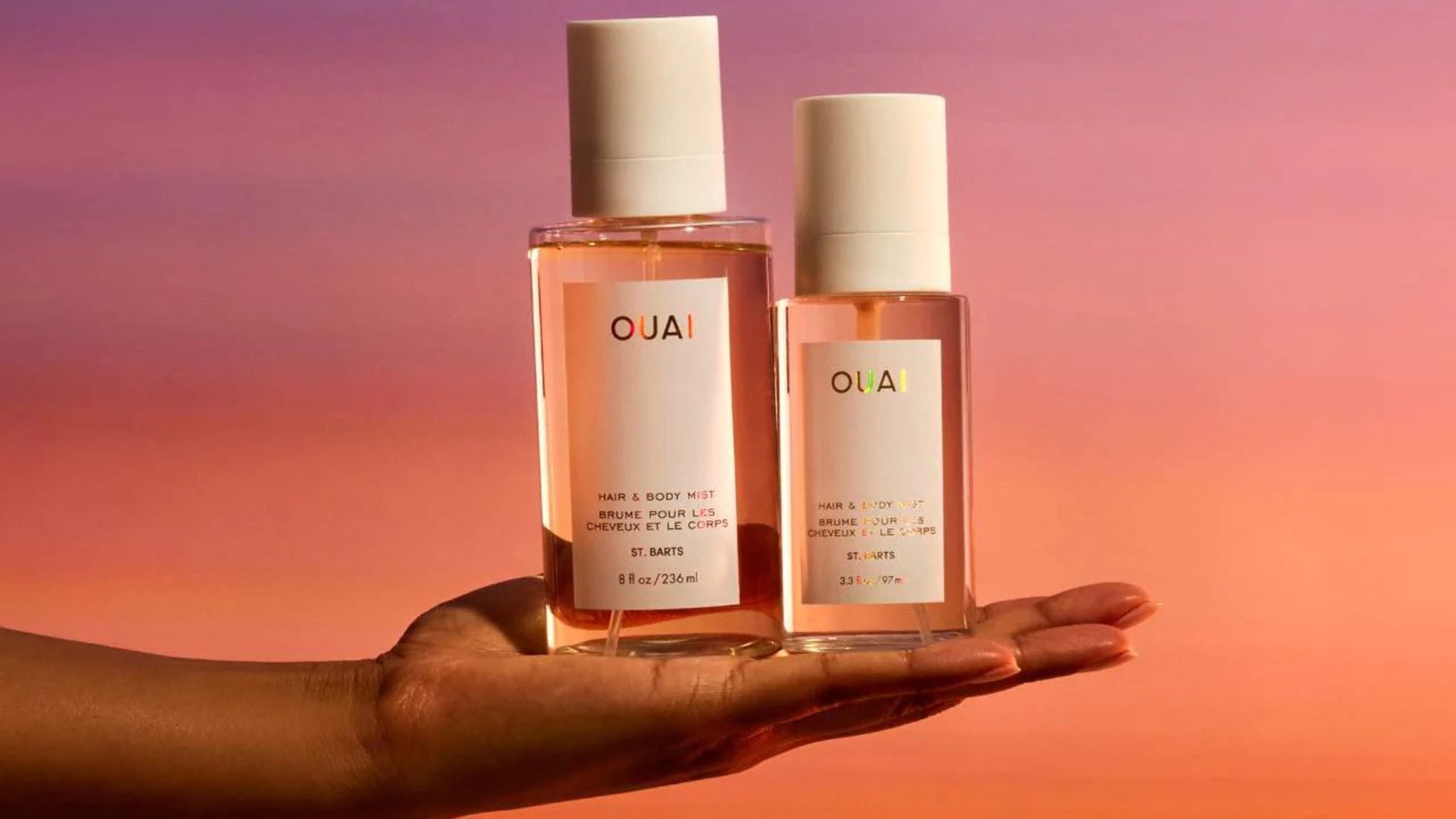 a hand holding two bottles of hair perfume with a sunset background
