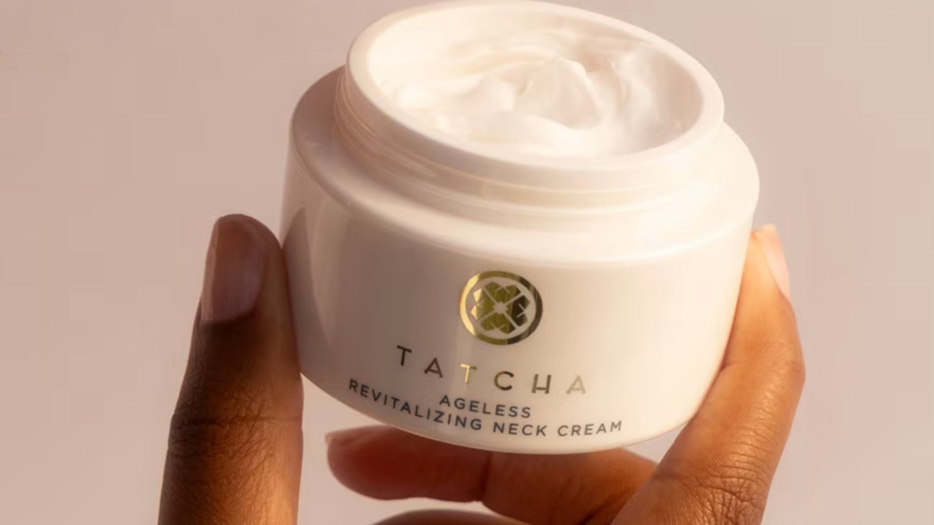A person holding up a tub of Tatcha neck cream.