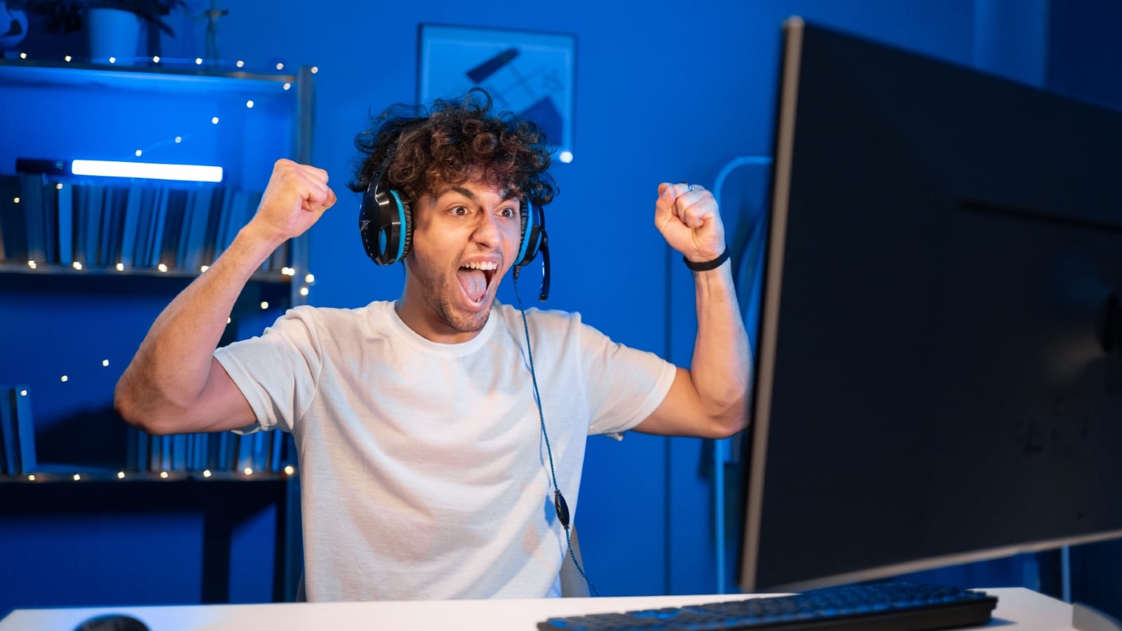 a person cheering while sitting at their computer with headphones on