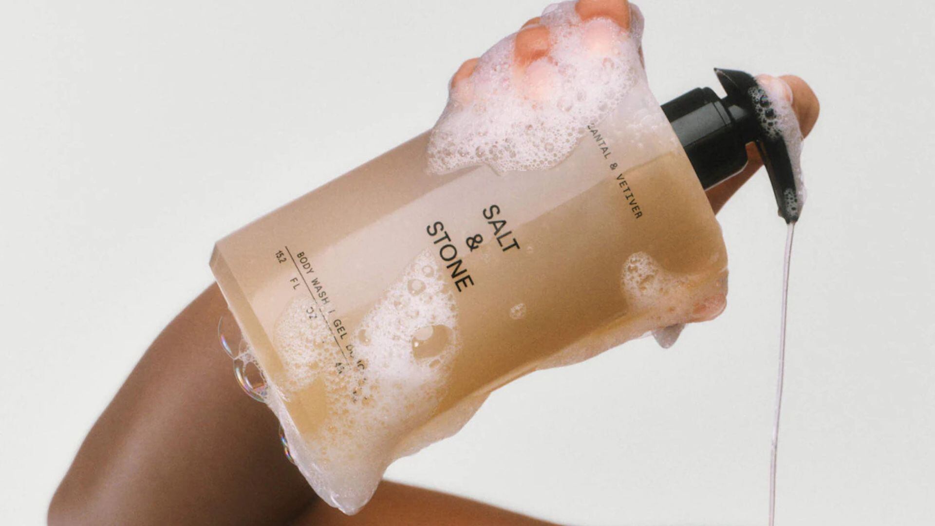 a person holding a bottle of body wash in the shower