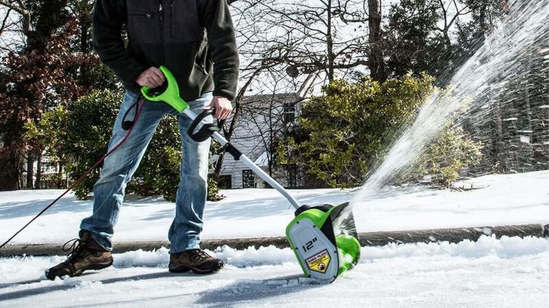 A person using an electric snow shovel on a driveway.