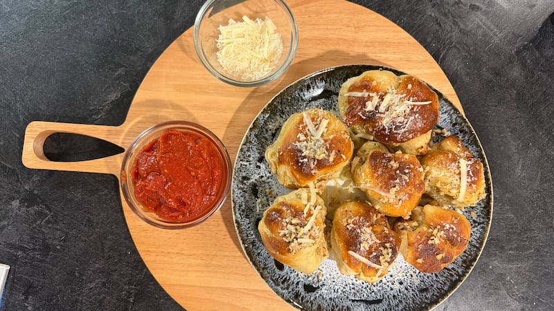 Garlic knots on a board with cheese and marinara dipping sauce
