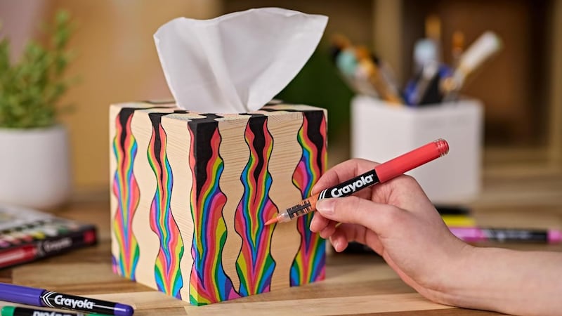 A person using a Crayola acrylic marker to decorate a wooden Kleenex box.
