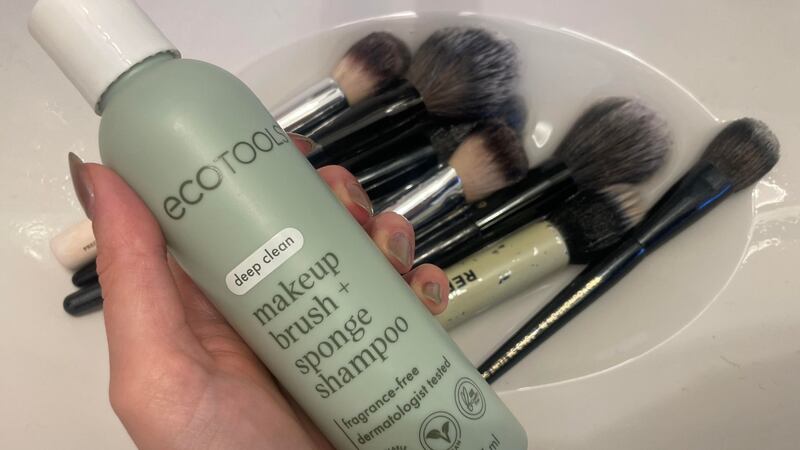 Alice holding a bottle of brush shampoo over a sink with her brushes in it