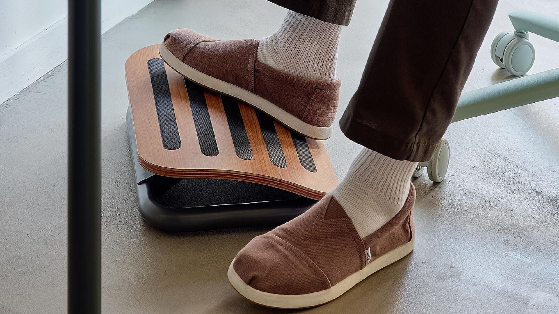 a person resting their foot on a wooden footrest under a desk