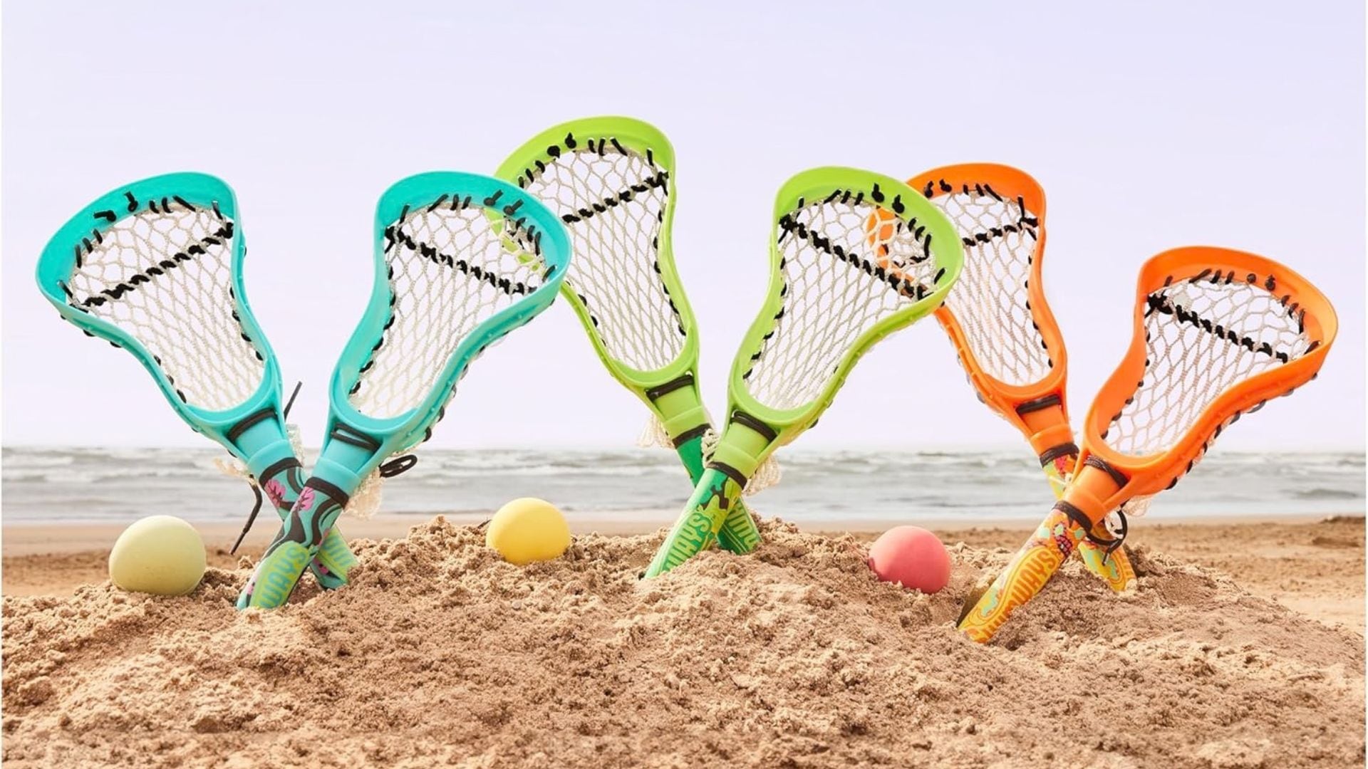 a set of six hydro lacrosse sticks and balls in the sand at a beach