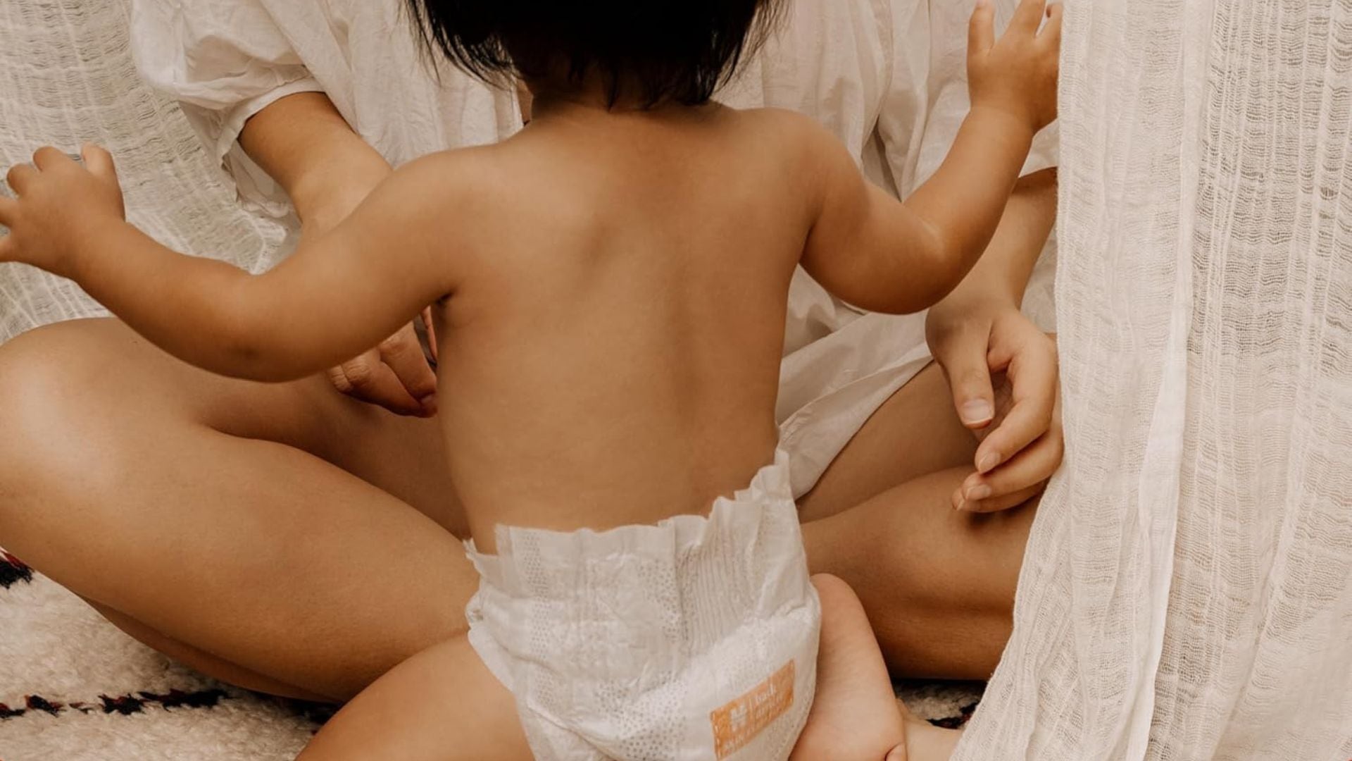 a parent sitting with a baby who is standing up wearing a diaper