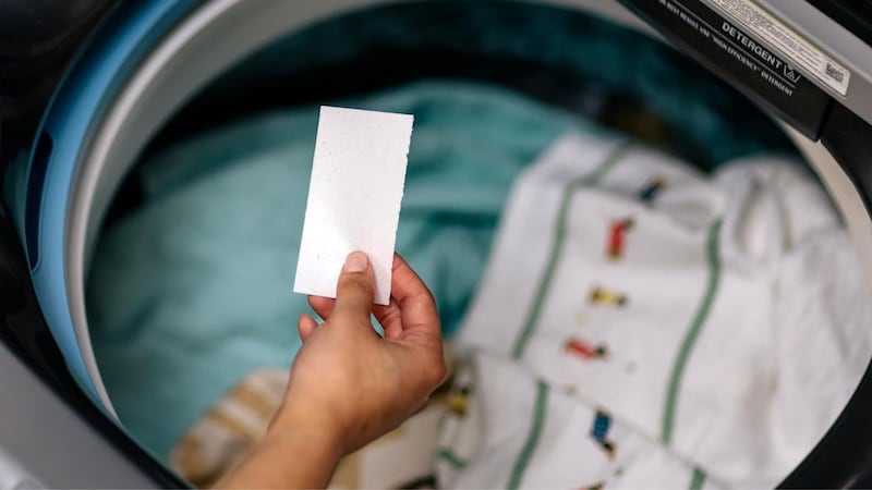 A person holding a Tru Earth detergent strip in front of a washing machine.