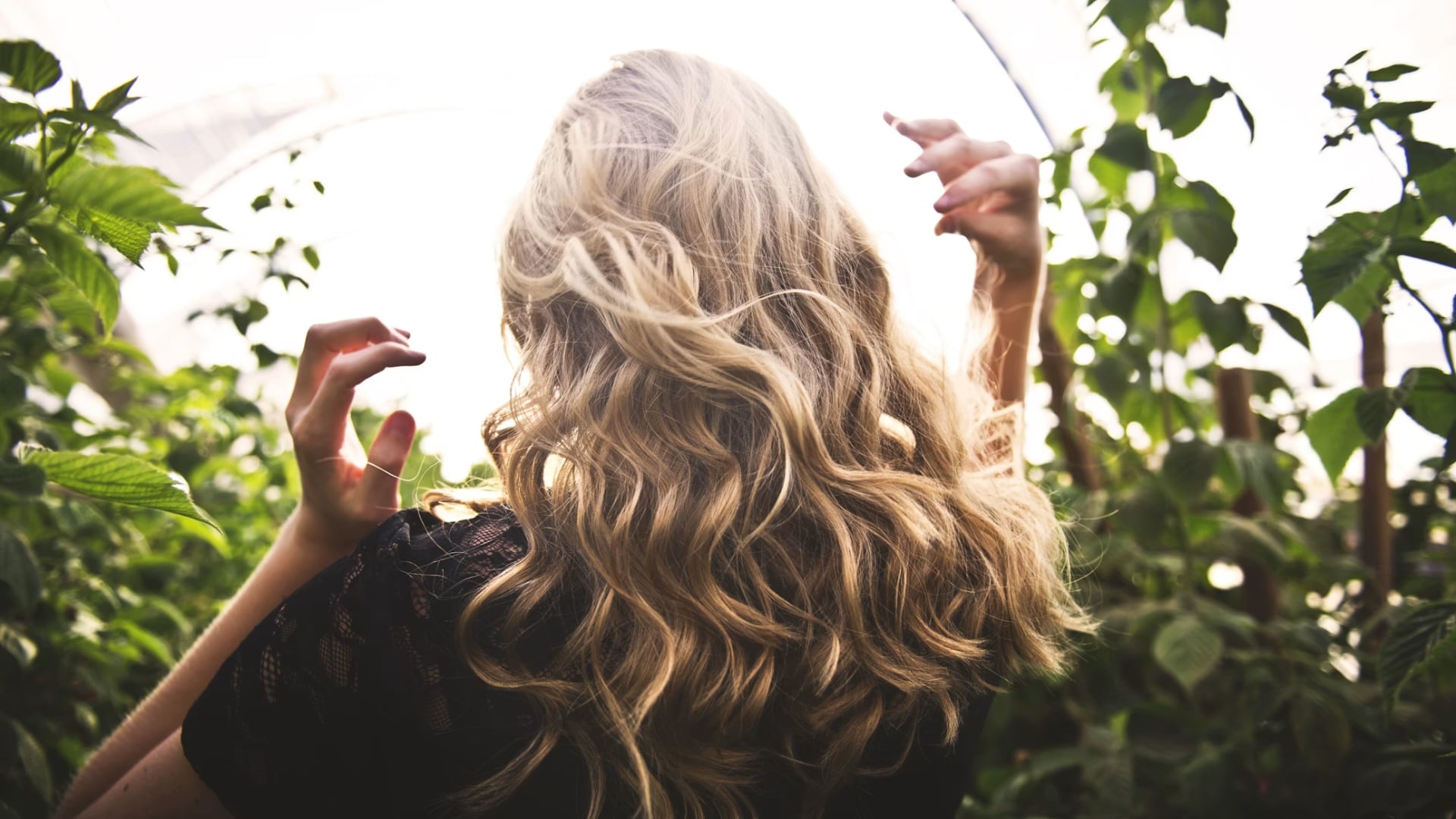 Blonde haired woman in black top surrounded by tall plants