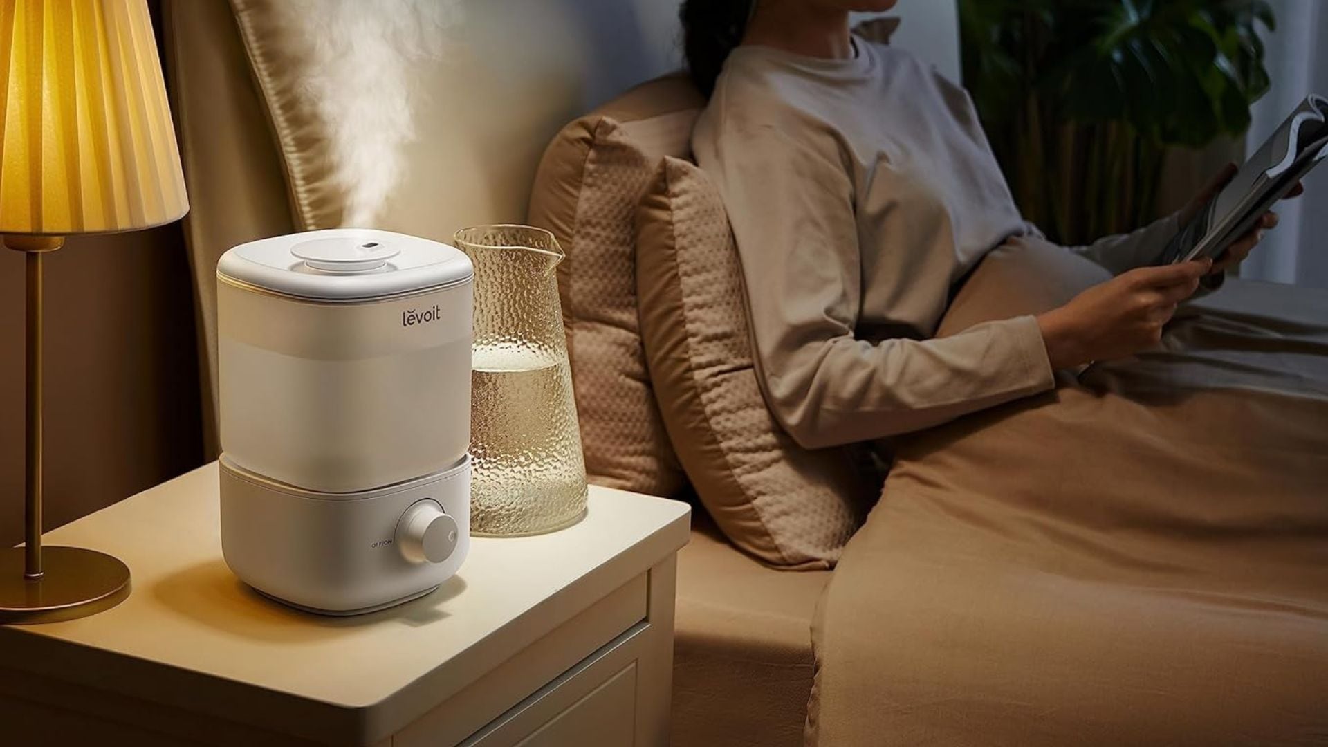 A person is lying in bed, and a humidifier is on a bedside table next to them.
