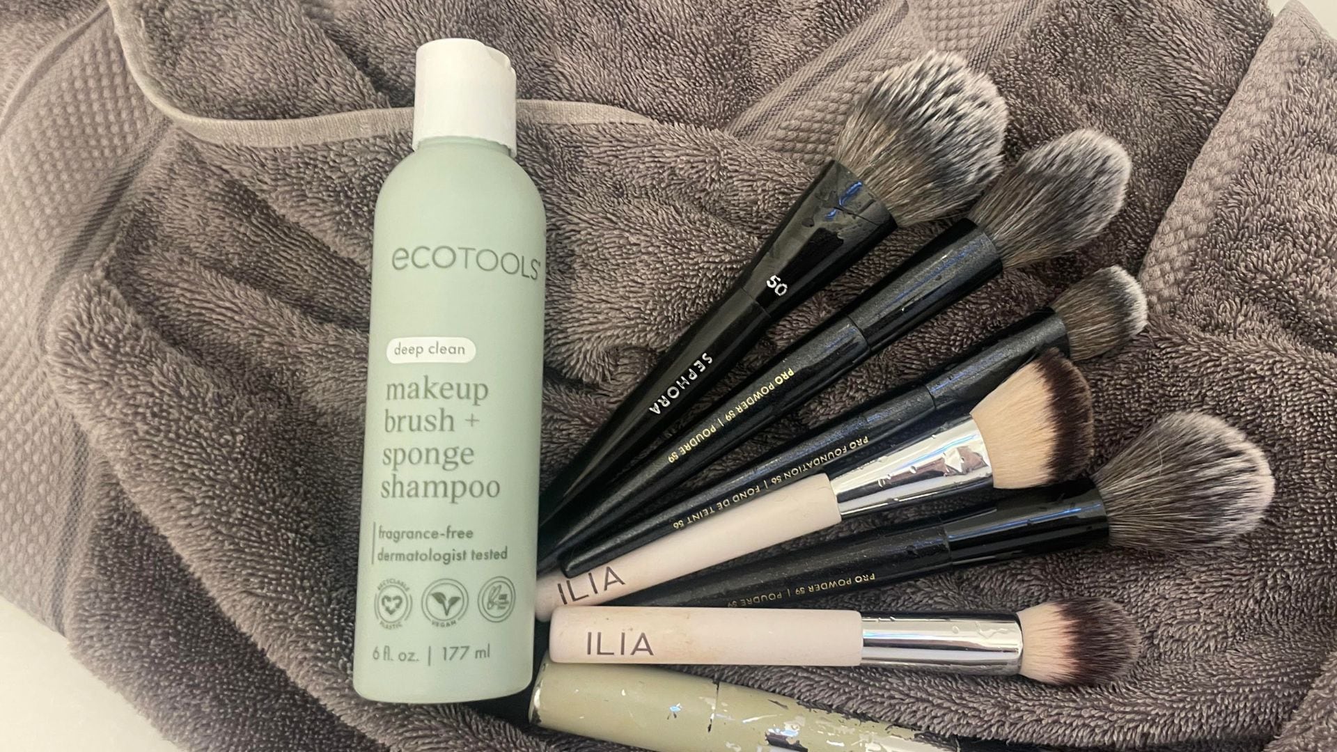 A bottle of makeup brush cleanser is next to fanned out brushes on a towel.
