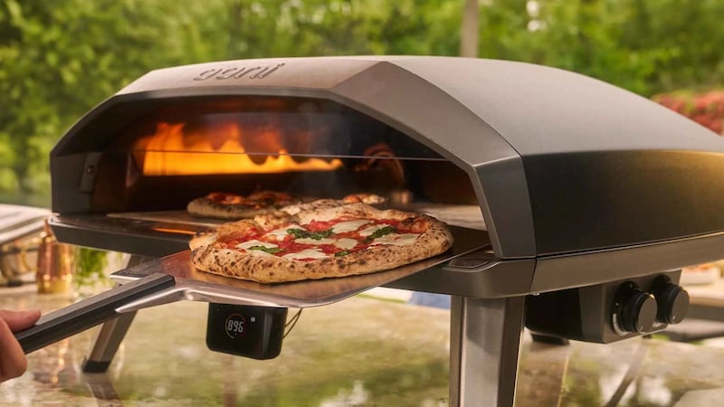 A person putting a pizza into an Ooni pizza oven.