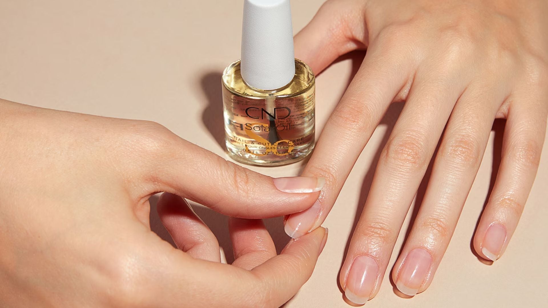 a person rubbing oil into their cuticles with the bottle of oil next to their hands