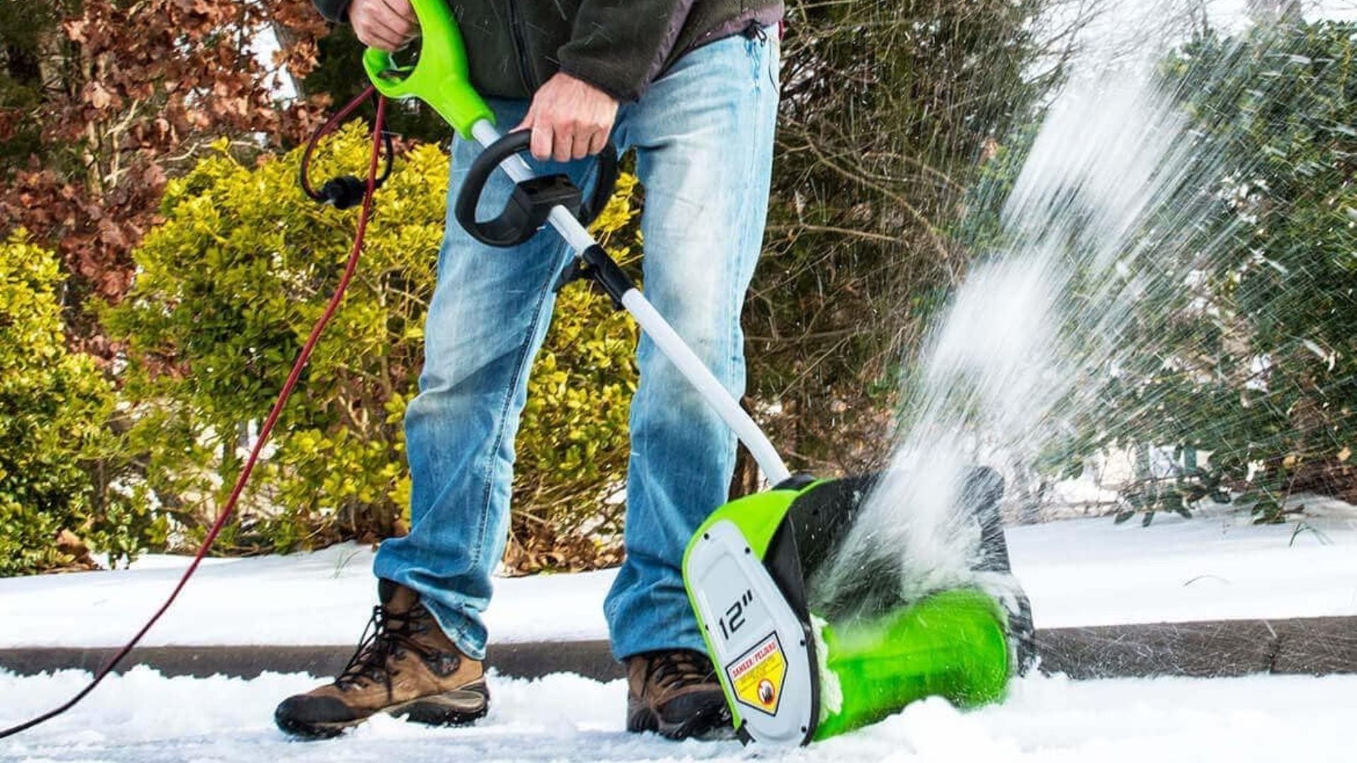 A person using a corded electric snow blower on their driveway.