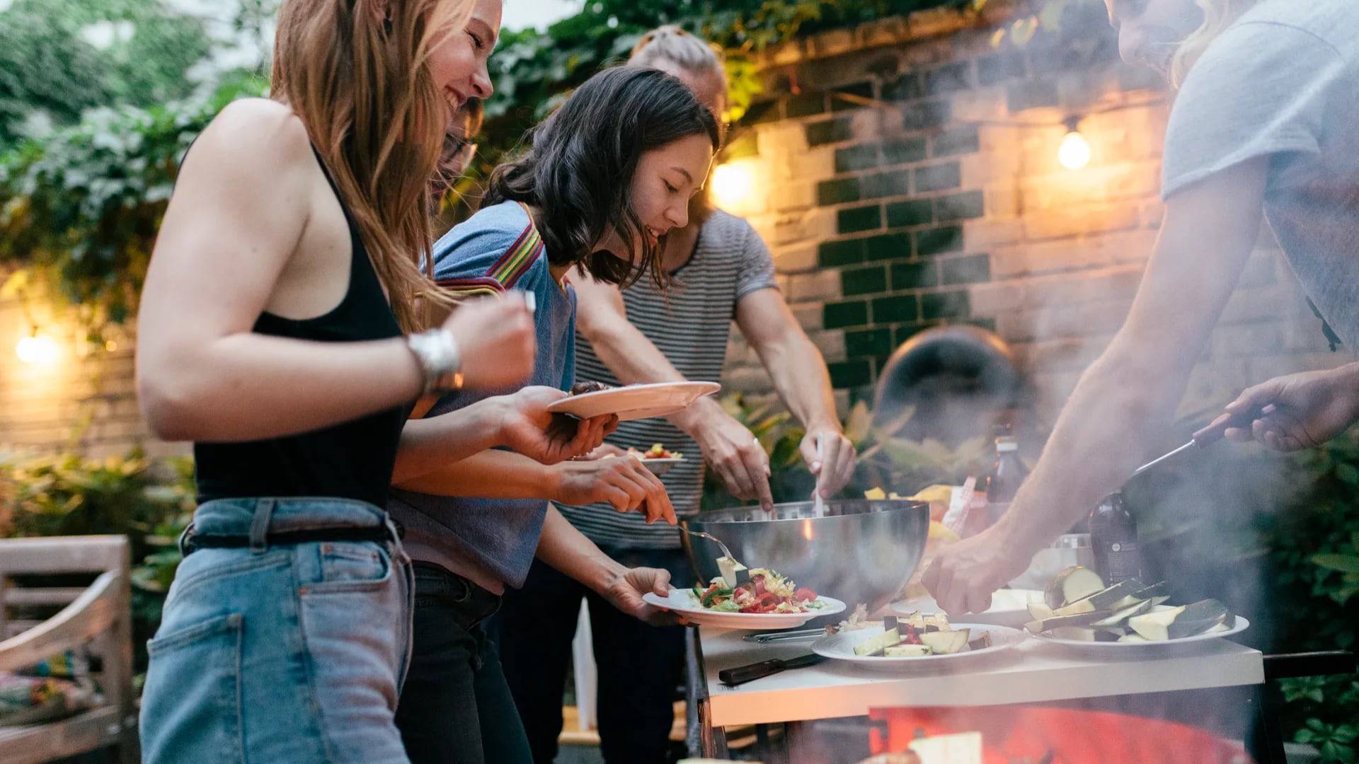 Group of friends preparing dinner plates next to a BBQ grill