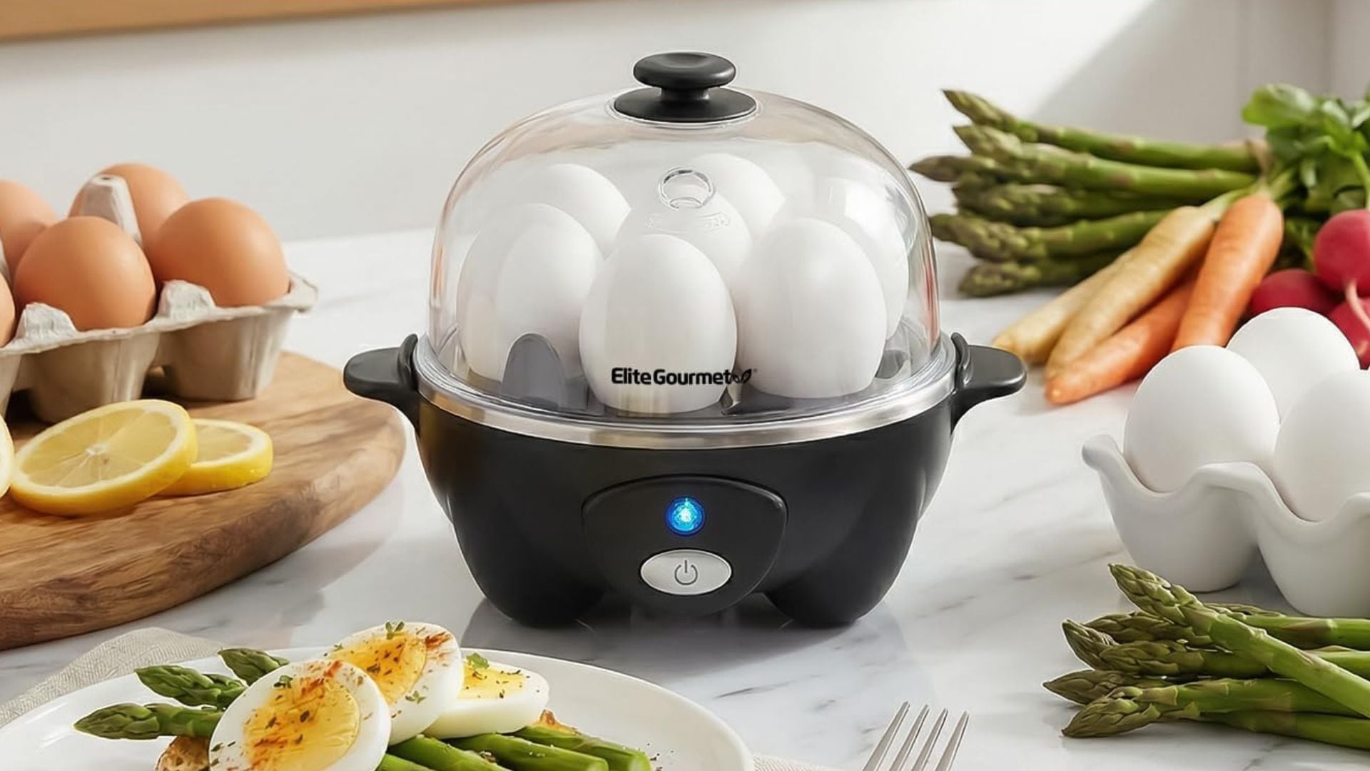 An Elite Gourmet egg cooker on a marble counter surrounded by food.