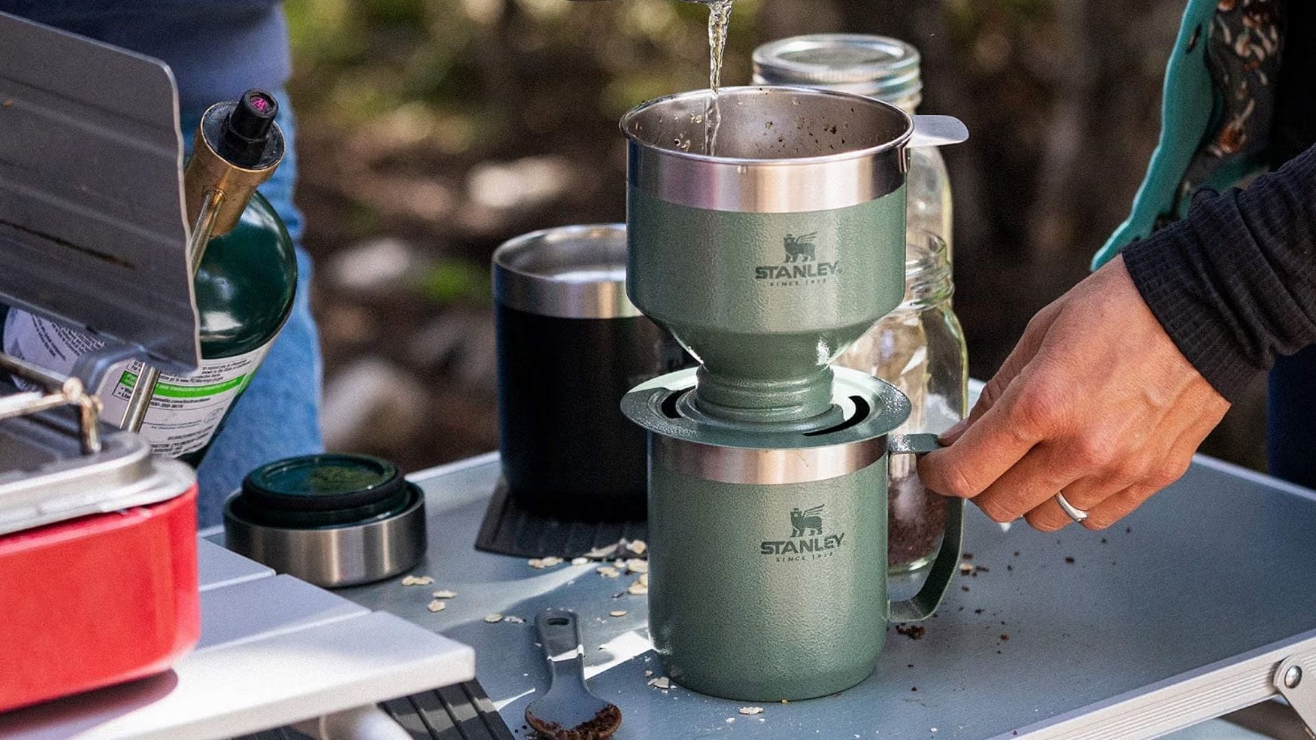 A person brewing coffee at a campsite with the Stanley Pour Over Coffee Set.