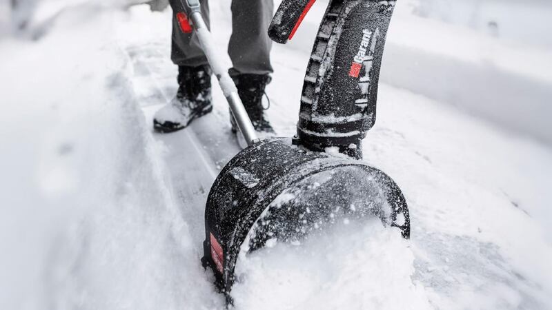 A person using an electric snow shovel on a snowy driveway.